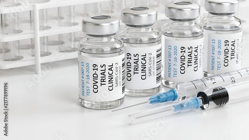 Close-up of covid-19 clinical trial vaccine vials in a row with medical syringes on a white laboratory table