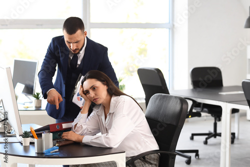 Angry male boss scolding female employee with folders in office