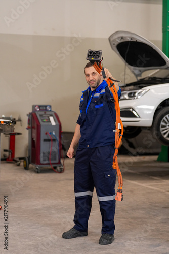 Technician mechanic vehicle workshop car repair diagnostic uniform tool service worker holding alignment sensor near lifted automobile during maintenance