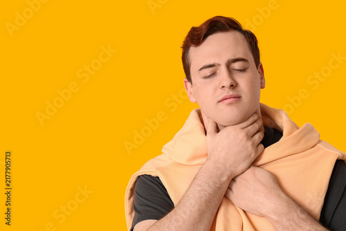 Young man with sore throat on yellow background