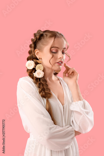 Beautiful young woman in dress with braid and roses on pink background