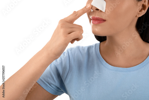 Young woman pointing at bandaged nose on white background, closeup. Plastic s...