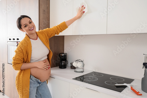 Young pregnant woman cleaning cupboard in kitchen