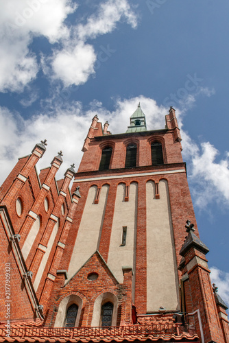 Foto Red brick church tower with a tall green spire rising above a tiled rooftop agai