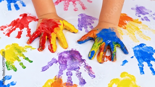 A child's hands covered in colorful paint making handprint art on a white background