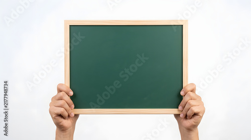 Two hands holding a rectangular green chalkboard with a light wooden frame against a plain white background, clean and minimalistic setup featuring blackboard, light brown, skin tone and human hands