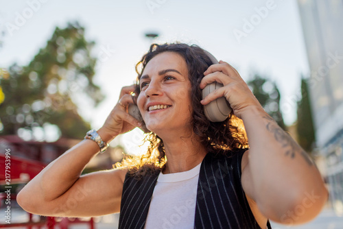 The positive young woman enjoys the sound in the headphones in the city center. A happy woman enjoying the music walking through the city street.