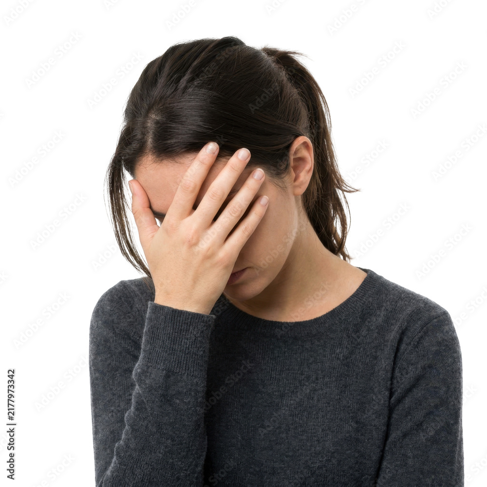 Fototapeta premium A young woman holds her hand over her face, showing distress and sadness.