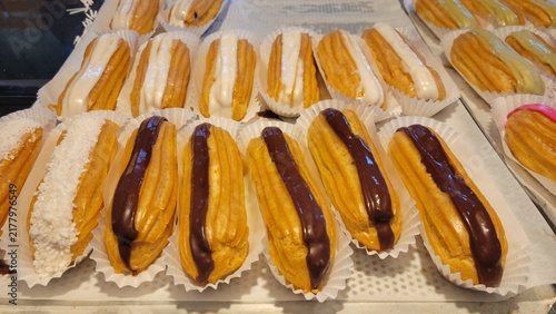 Quadro su tela Rows of chocolate and vanilla eclairs in paper trays at bakery pastry display