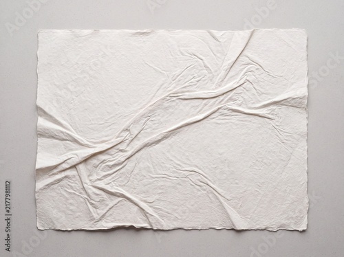 Crumpled white paper texture with deckle edges. Wrinkled handmade paper sheet on gray background. Creased parchment for stationery mockups.