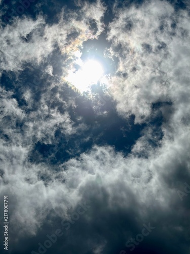Bright sun shining through dramatic dark and white clouds with patches of blue sky. Powerful weather background with light rays and copy space.