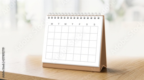 Blank desktop spiral desk calendar standing on wooden table in bright minimalist office with soft natural lighting for business planning scheduling appointments and time management concepts copy space
