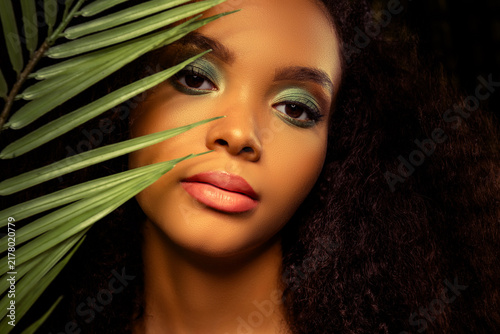 Fotografie Glorious beautiful young woman with natural curls and vibrant makeup among tropi