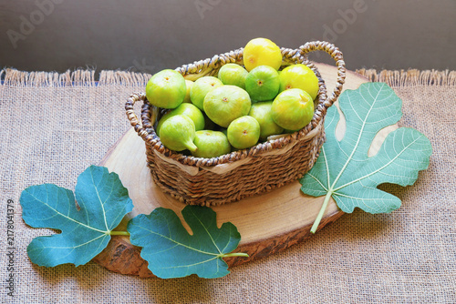 Ripe figs in small basket and leaves of fig tree on table