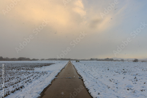 Narrow road through snow covered fields in countryside as clouds clear at sunrise
