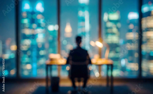 A businessman sitting at a desk in a modern office with a city skyline view at night. The lights of skyscrapers create a vibrant, atmospheric background.