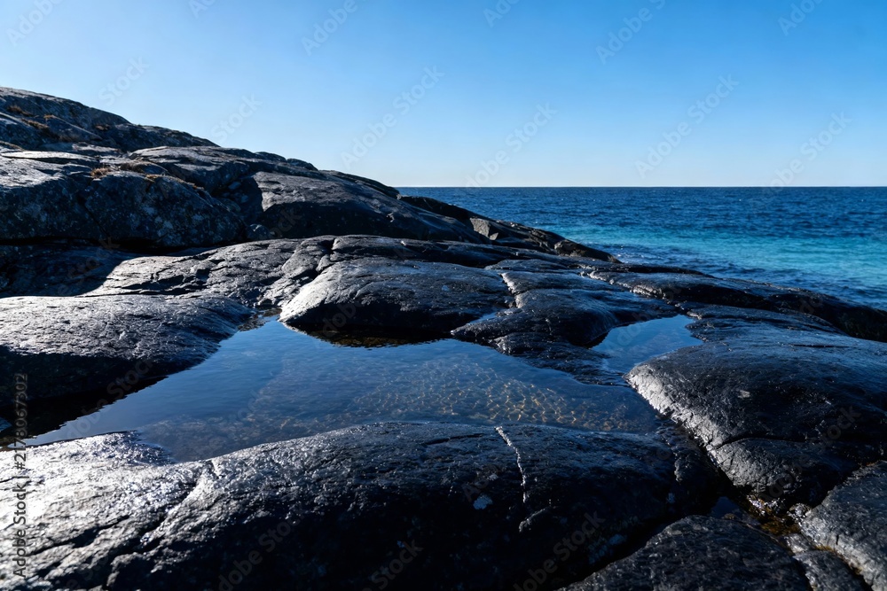 Fototapeta premium Rocky shoreline with tide pools reflecting clear blue sky and ocean