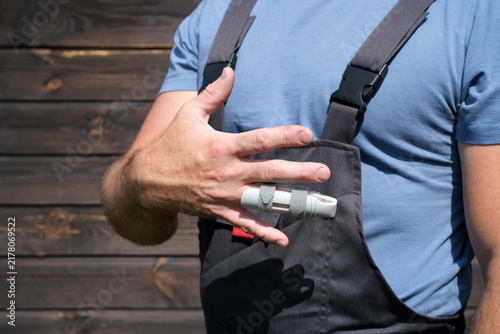 Obraz na plátně Worker in protective workwear showing injured finger with splint after workplace