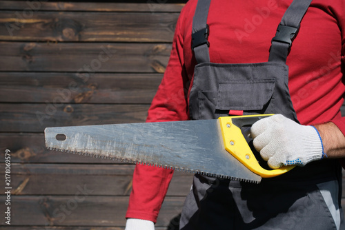 Fotografía Red clad worker holding handsaw in protective gloves and dark work overalls near