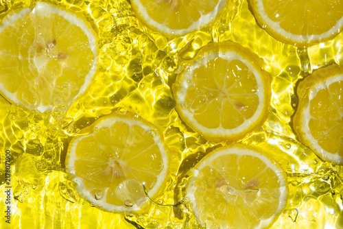 Fotografía Fresh citrus lemon slices splashing in bright water background.