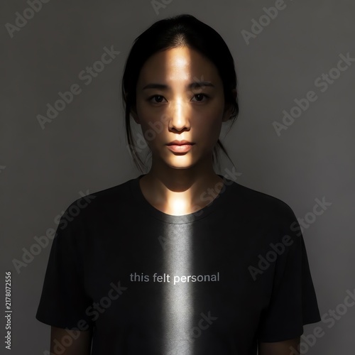 Dramatic portrait of a serious young asian woman with a vertical beam of light on her face and shirt
