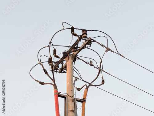 High-angle view of a concrete utility pole with complex electrical wires, lines, and insulators against a clear bright sky.