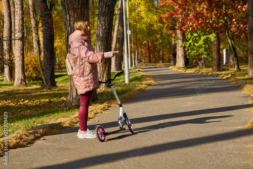 Woman in pink jacket with a scooter points in direction ,autumn park