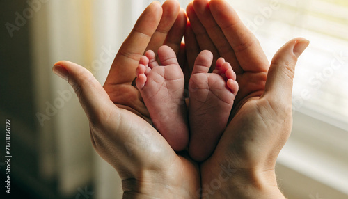 Tiny newborn baby feet held gently in adult hands.