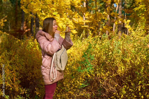 Autumn make up. Woman paints lips among golden foliage in forest park