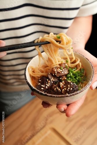 Woman holding Asian ramen noodle bowl with chopsticks close up
