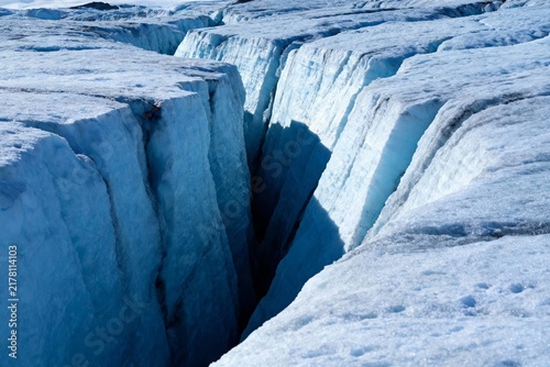 Deep crevasse in a glacier with blue ice walls and snow-covered surface