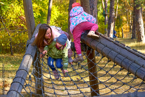 Mother with children playing on gladiator rope net, autumn park