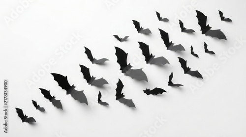 A swarm of black paper bats flying in a diagonal pattern across a plain white surface creating a minimalist and spooky holiday atmosphere
