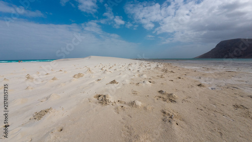 Quadro su tela Empty sandy beach beneath cloudy blue sky