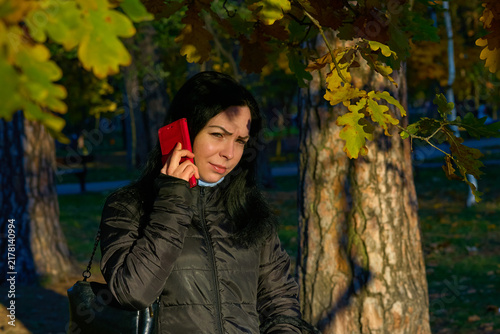 Woman calling,talking,listening while walking in an autumn park