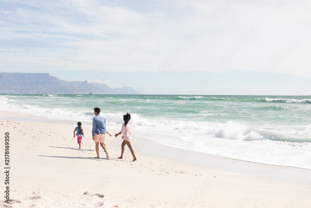 Obraz premium Full length of multiracial parents walking behind son on shore at beach during sunny day