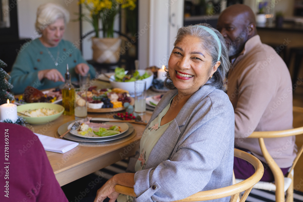 Obraz premium Happy senior woman celebrating with friends at christmas dinner in sunny dining room