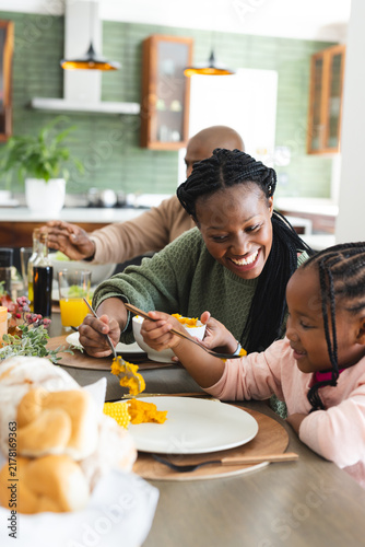 Happy african american mother serving food for daughter at thanksgiving dinner