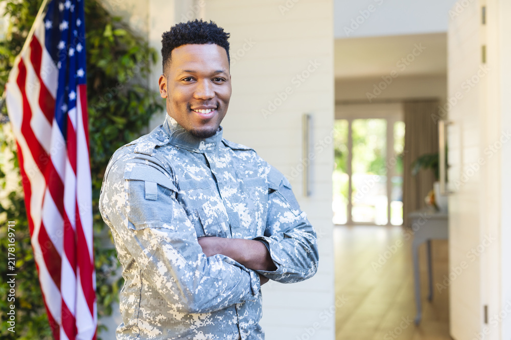 Obraz premium African american male soldier standing with arms crossed outside home with usa flag, copy space
