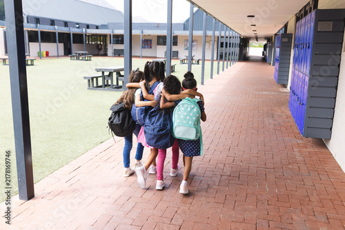 In school, four young girls are walking closely together outdoors