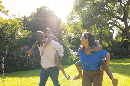 Playing in garden, multiracial parents giving piggyback rides to daughters, smiling and laughing