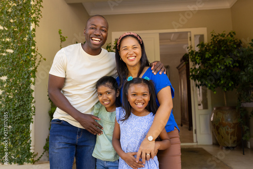 Smiling family of four with daughters standing together outside home, enjoying quality time