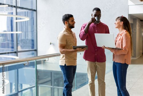 Discussing work, colleagues using laptop and tablet while standing in office hallway