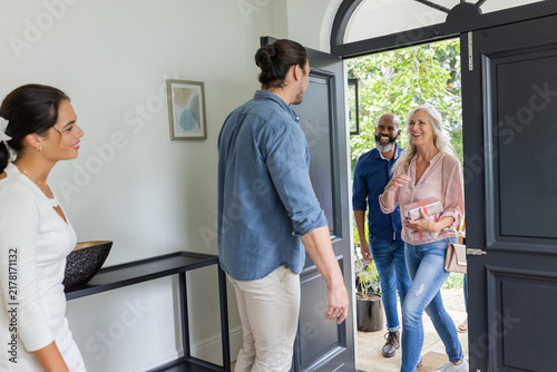Welcoming guests at home, smiling couple greeting friends at front door