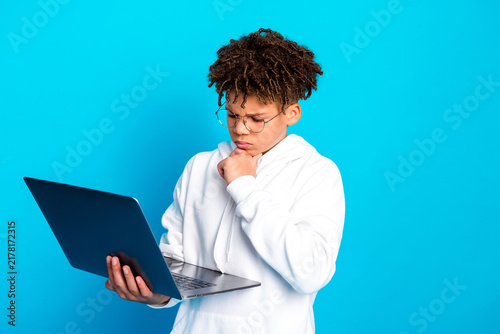 Obraz na płótnie Teen boy studying with laptop, thoughtful expression while holding computer agai