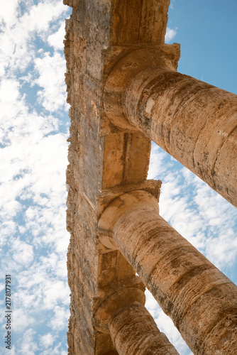 Vertical steep low-angle shot of Doric capitals and stone architrave against blue sky with clouds in Segesta, Sicily, Italy
