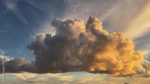 Huge cumulus storm cloud glowing in golden light during sunset over scenic sky. Dramatic atmospheric cloudscape illuminated by warm sun rays in evening