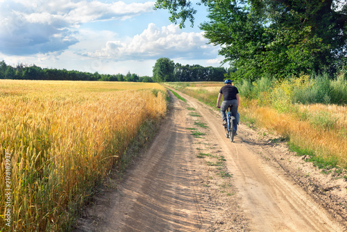 Young cyclist riding blue bicycle along dirt road near ripe wheat field