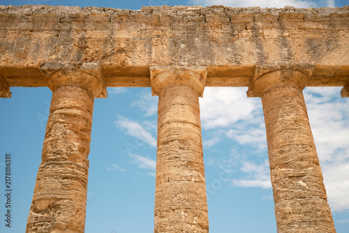 Horizontal low-angle view of three Doric column capitals and stone architrave against blue sky with clouds in Segesta, Sicily, Italy
