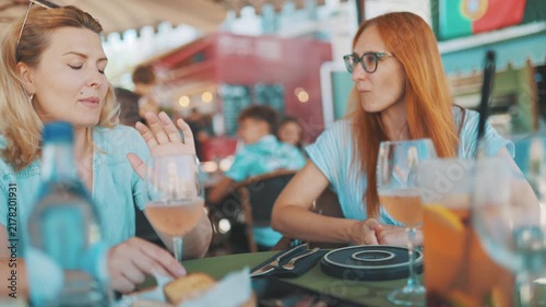 Two friends have a conversation at a cafe in a sunny outdoor setting in Portugal